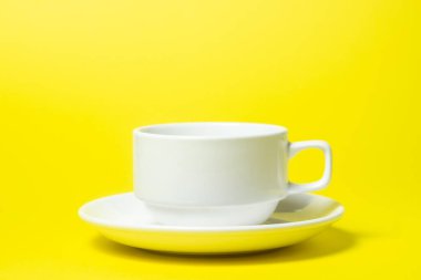 Sarı arka planda bir fincan üzerinde boş bir fincan. Fincan ve çay tabağı beyazdır. Çay takımı.
