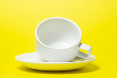 Sarı arka planda bir fincan üzerinde boş bir fincan. Fincan ve çay tabağı beyazdır. Çay takımı.