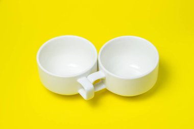 Sarı arka planda beyaz bardaklar. İki beyaz bardak yan yana yatar.