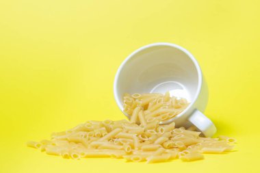 Sarı arka planda makarna. Makarna bardaktan döküldü. İtalyan Mutfağı