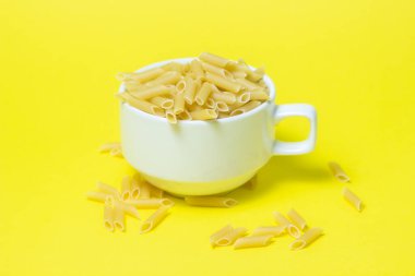 Sarı arka planda makarna. Makarna dolu bir fincan. İtalyan Mutfağı
