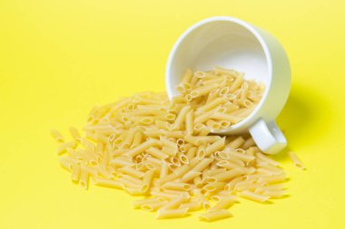 Sarı arka planda makarna. Makarna bardaktan döküldü. İtalyan Mutfağı