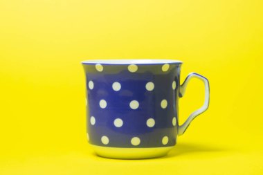 Beyaz benekli mavi bardak. Sarı arka planda bir kupa. renkli yemekler.