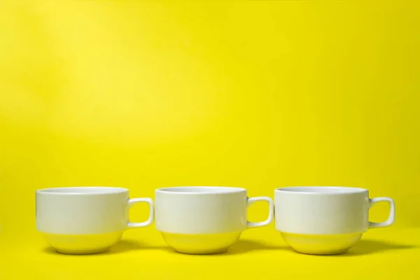 White cups on a yellow background. Three white cups are in a row. A tea set.