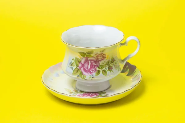 Tea cup and saucer on a yellow background. The service is decorated with flowers.
