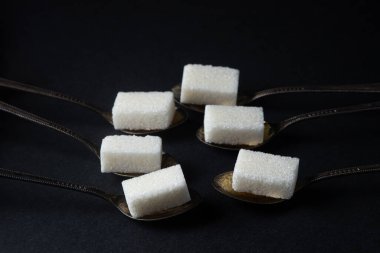 Siyah arka planda şeker. Küp şekerli kaşıklar. Kaşıklar yan yana uzanıyor.