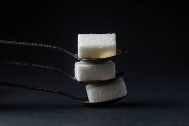 Siyah arka planda şeker. Küp şekerli kaşıklar. Kaşıklar birbirinin üstüne yatar.