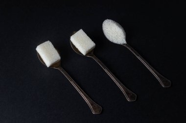 Siyah arka planda şeker. Şeker küpleri ve granüllü şeker. Şeker kaşıkları