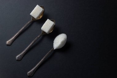 Siyah arka planda şeker. Şeker küpleri ve granüllü şeker. Şeker kaşıkları