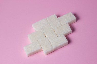 Pembe arka planda küp şekerler. Şeker küpleri bir şekle sokulur..