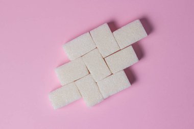 Pembe arka planda küp şekerler. Şeker küpleri bir şekle sokulur..