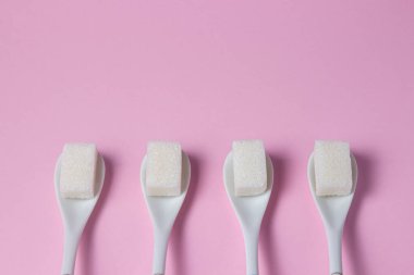 Pembe arka planda küp şekerler. Şeker küpleri kaşıkların üzerinde yatar. Şekerli kaşıklar sıraya dizildi.