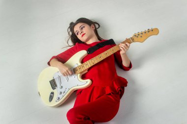 Kırmızı elbiseli kız. Kız elektro gitar çalıyor. Kız beyaz zeminde yatıyor.