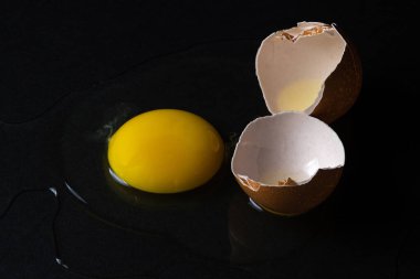 Siyah arka planda yumurta. Kırık tavuk yumurtası. Yumurta sarısı masaya döküldü.