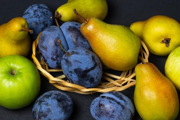 Fruit on a black background. Plums, pears and apples lie side by side. Healthy fruits