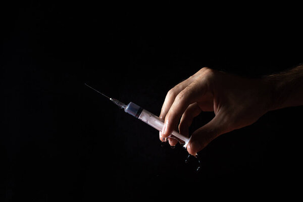 Hand holds a medical syringe on a black background. Water drips from the syringe
