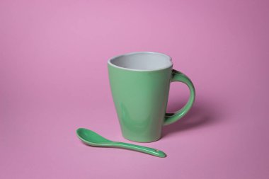 Pembe arka planda yeşil kupa. Bir kupa ve çay kaşığı.