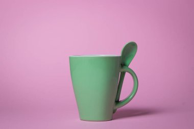 Pembe arka planda yeşil kupa. Bir kupa ve çay kaşığı.