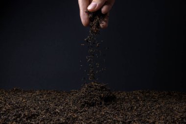Yaprak çayı. Bol bol çay. El, siyah arka planda gevşek çay serper.