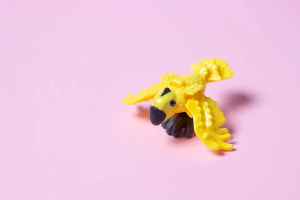 おもちゃのオウム ピンクの背景に黄色いおもちゃのオウム プラスチックパーロット — ストック写真