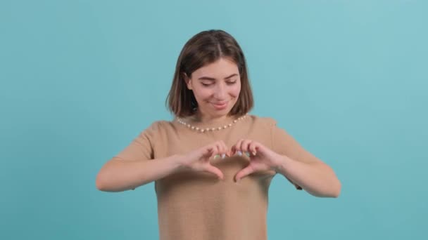 Mujer feliz poner hacer con los dedos en forma de corazón, aislado sobre fondo turquesa. — Vídeo de stock