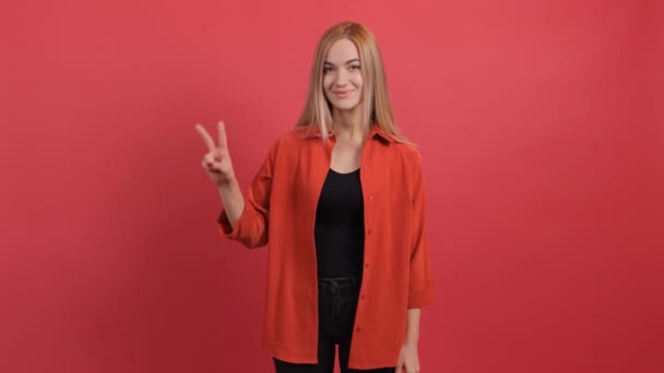 Joven sonriente mostrando signo de paz sobre fondo rojo. — Vídeo de stock