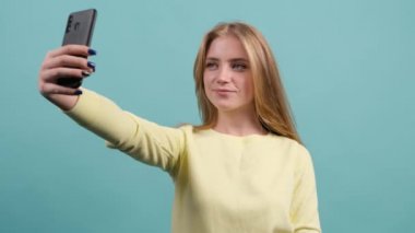Sarışın genç kadın turkuaz arka planda selfie çekiyor..