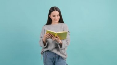 Turkuaz arka planda izole edilmiş kitap okuyan güzel bir kadın..