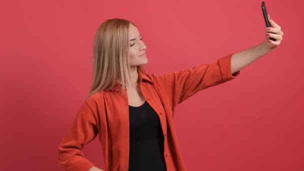 Lustige junge blondhaarige Frau macht Selfie auf rotem Hintergrund. — Stockvideo