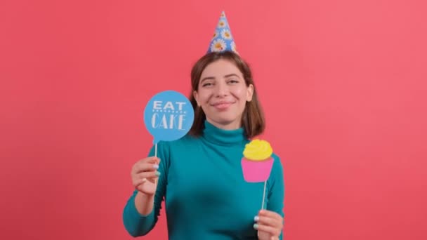 Happy młoda kobieta w partii kapelusz gospodarstwa akcesoria urodzinowe na czerwonym tle. — Wideo stockowe
