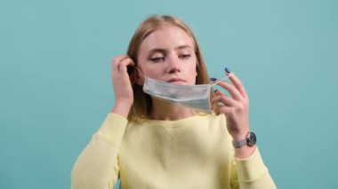 Genç bir kadın turkuaz bir arka planda tıbbi maske takıyor..