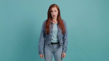 Turkuaz stüdyo arka planında kafası karışmış bir kadın el ele tutuşuyor..