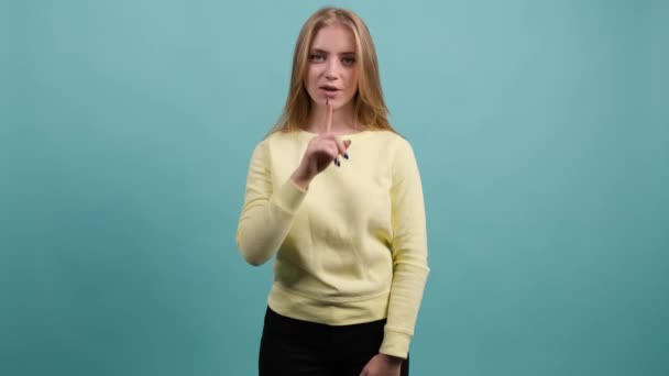 Smiling girl showing to be quiet with finger, isolated over turquoise background. — Stock Video