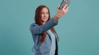 Turkuaz arka planda selfie çeken komik, genç, kızıl bir kadın..