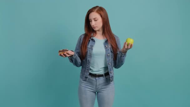 Ung kvinna väljer mellan äpple och munk, flickan är förvirrad i sitt val — Stockvideo