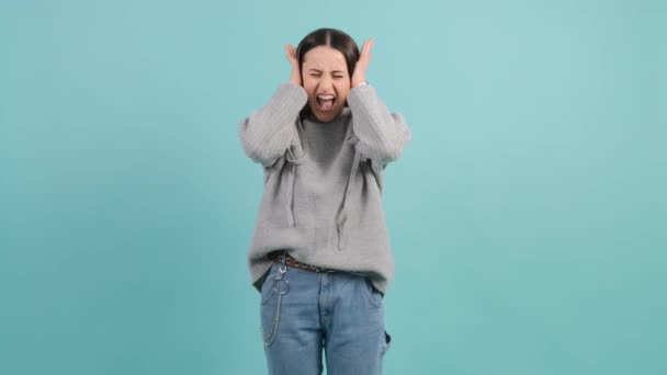 Confused woman holding hands on ears and shouts over turquoise studio background — Stock Video