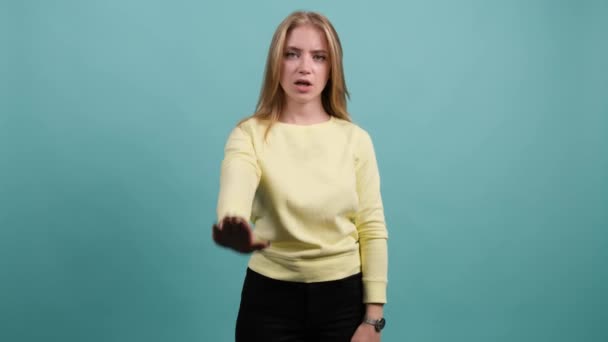 Jeune femme faisant un geste d'arrêt avec sa main, isolée sur fond turquoise. — Video
