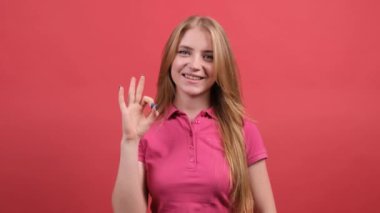 Mutlu genç bir kadın kırmızı arka planda izole edilmiş parmaklarıyla ve göz kırparak işaret veriyor..