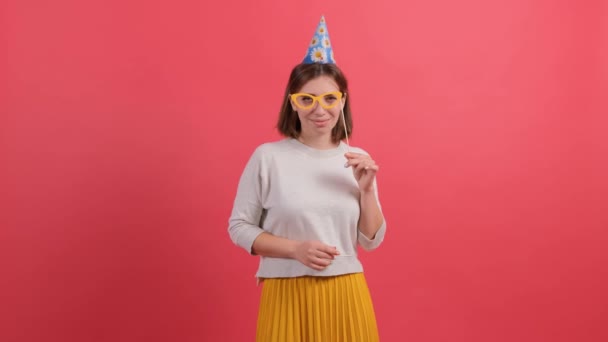 Jovem feliz em chapéu de festa segurando acessórios de aniversário no fundo vermelho. — Vídeo de Stock