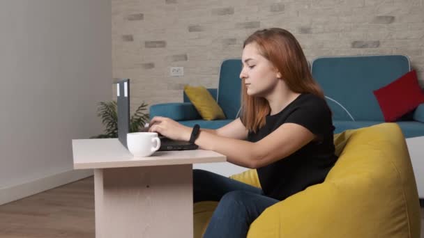 Jonge vrouw is het drinken van een kopje koffie terwijl werkt op de laptop van thuis kantoor. — Stockvideo