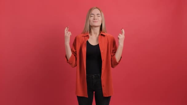 Mujer joven que mantiene los dedos cruzados, aislados sobre fondo rojo. — Vídeo de stock