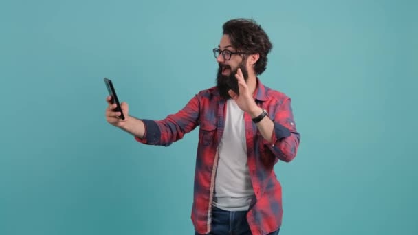 Retrato de un hombre barbudo hablando en videollamada y saludando con la mano haciendo un gran gesto. — Vídeos de Stock