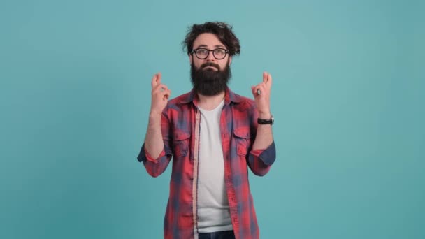 Young man that keeps fingers crossed, isolated over turquoise background. — Stock Video