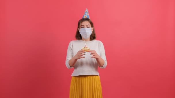 Сумна дівчина з медичною маскою на обличчі намагається підірвати свічку з торта . — стокове відео