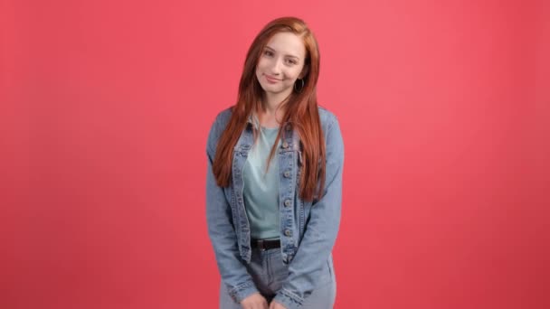 Mujer joven y bonita mirando a la cámara con una sonrisa, sobre fondo rojo. — Vídeos de Stock