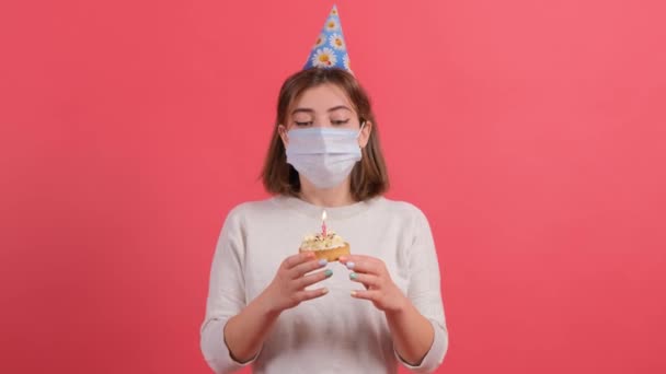 Jeune femme avec masque médical sur le visage essayant de souffler la bougie sur le gâteau. — Video
