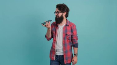 Sakallı adam sesli masaj yaparken akıllı telefonunu ağzının yanında tutuyor.