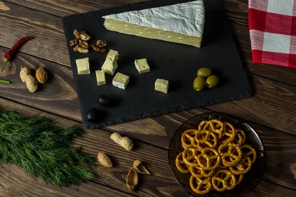 Camembert cheese. cheese dish with olives, herbs, snacks on an old black wooden table. brie cheese. Food for wine and romance, cheese delicacies. Menu design. napkin with a scottish pattern