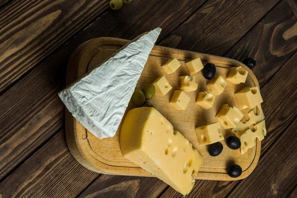 Tasting a cheese dish with olives on an old black wooden table. Food for wine and romance, cheese delicacies. Menu design horizontal. View from above.
