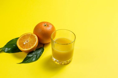 Portakal suyu ve dilimlenmiş portakal suyu. Bir bardak portakal suyu, bir portakal ve sarı arka planda dilimlenmiş bir portakal.